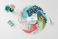 Feed My Soul charm pack squares fanned out with fresh flowers and sewing notions in a bright modern setting
