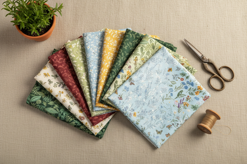 Botanical Garden jelly roll strips fanned out with botanical accents on a linen surface